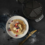 Macchina per waffle in acciaio inox con waffle decorati su piatto e frutta fresca