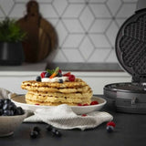 Macchina per waffle in acciaio inox con waffle dorati serviti su un piatto con frutti di bosco freschi