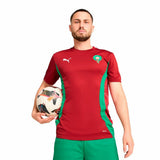 Maglia calcio uomo Puma Marruecos in rosso e verde con logo Puma, indossata da un uomo che tiene un pallone.