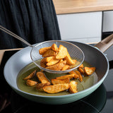 Schiumarola in metallo resistente con patate fritte dorate in una padella moderna