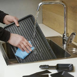 Persona che pulisce la griglia della raclette Severin RG9670 sotto l'acqua corrente nel lavandino